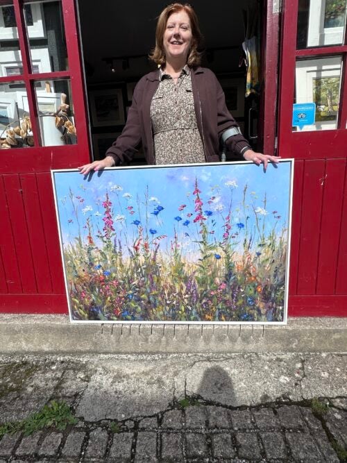 Karen standing at the door of Karen Wilson Art with a large canvas print called field of dreams